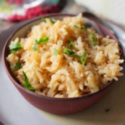 a single serving of rice pilaf in a bowl next to half of an onion.