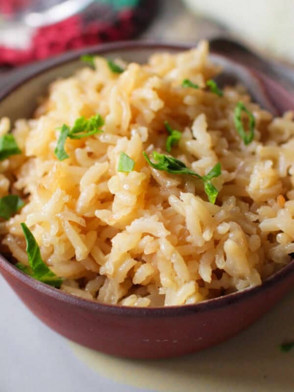 a single serving of rice pilaf in a bowl next to half of an onion.