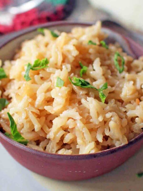a brown bowl filled with rice pilaf topped with chopped parsley.