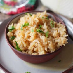 a brown bowl filled with rice pilaf topped with chopped parsley