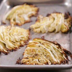 four roasted cabbage wedges on a silver baking sheet.