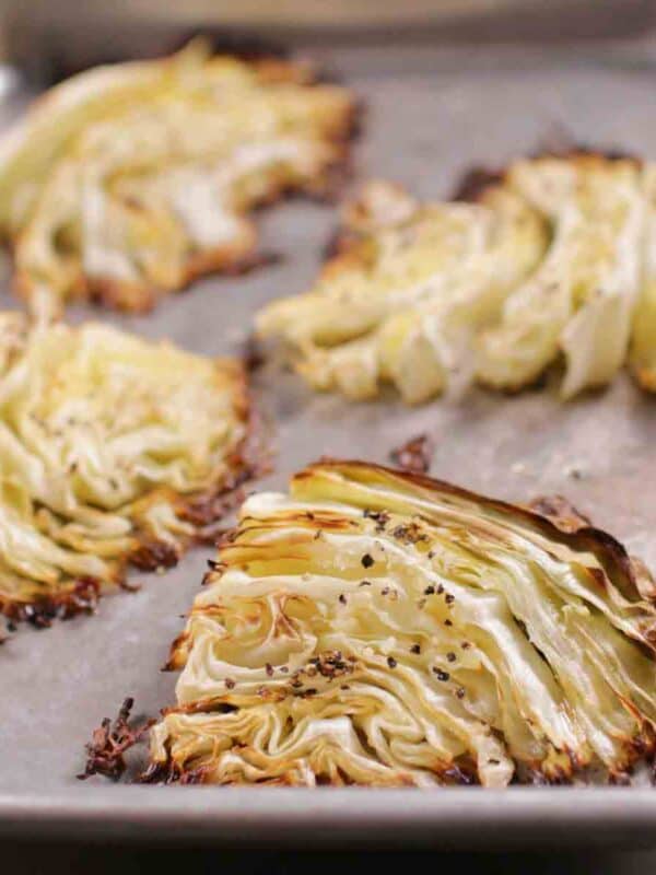 four roasted cabbage wedges on a silver baking sheet.