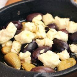 roasted garlic with olives and feta in a black baking dish