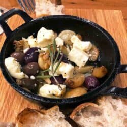 garlic and olives in a small dish sitting on a brown cutting board.