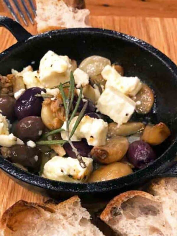 garlic and olives in a small dish sitting on a brown cutting board.