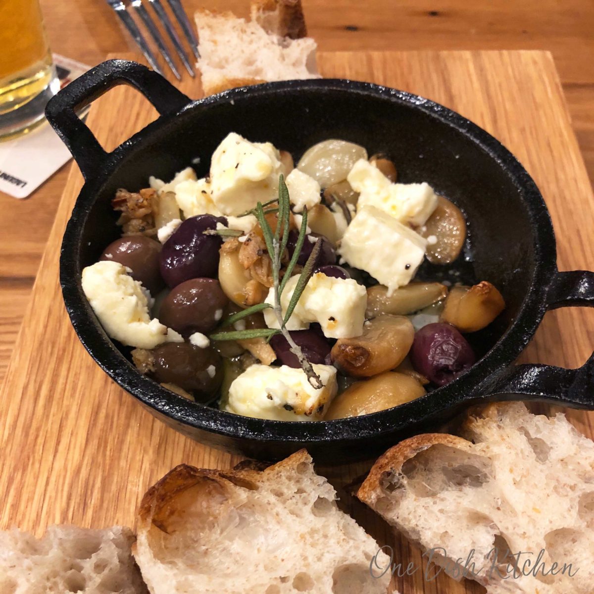 garlic and olives in a small dish sitting on a brown cutting board