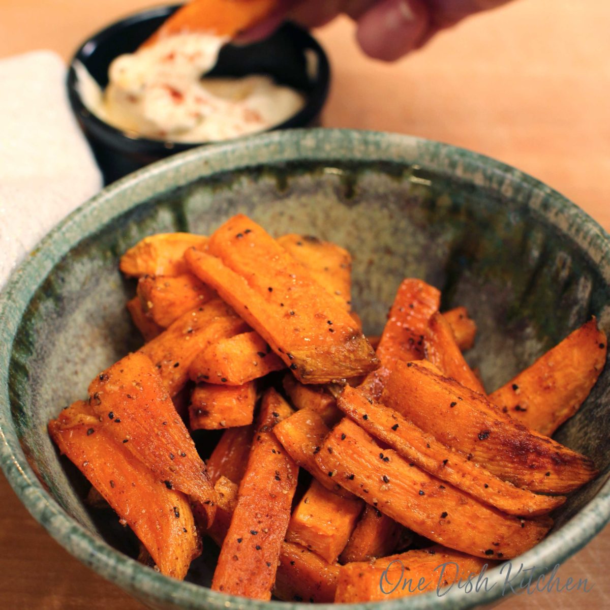 a bowl of sweet potato fries with a black bowl of mayonnaise in the background