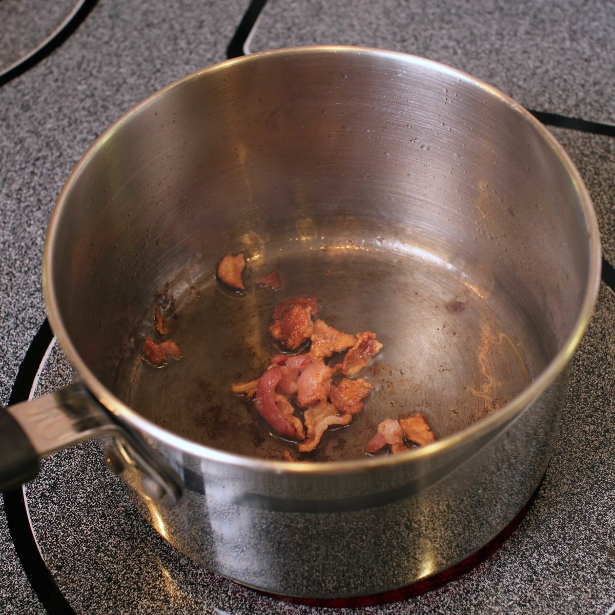 bacon pieces in a silver pot on a stove.
