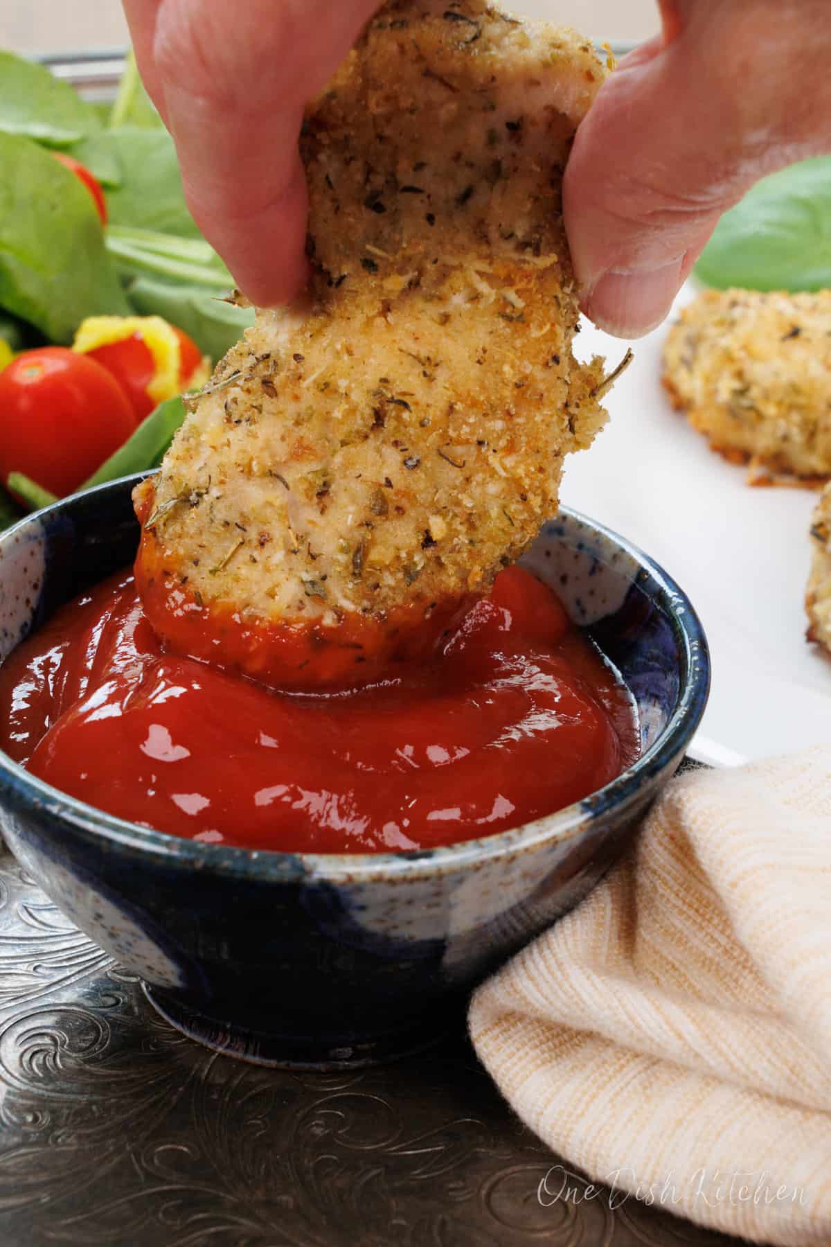 one chicken tender being dipped in a bowl of ketchup