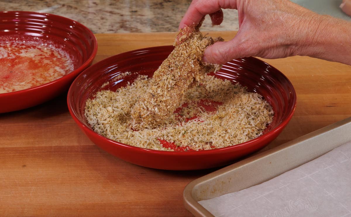 dredging one chicken strip in a bowl of breadcrumbs