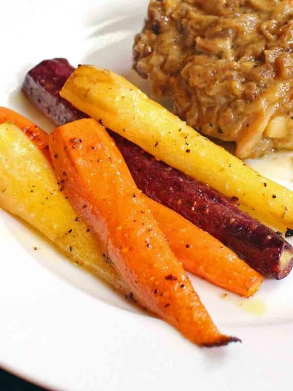 roasted carrots on a white plate on a silver tray next to chicken with onions.