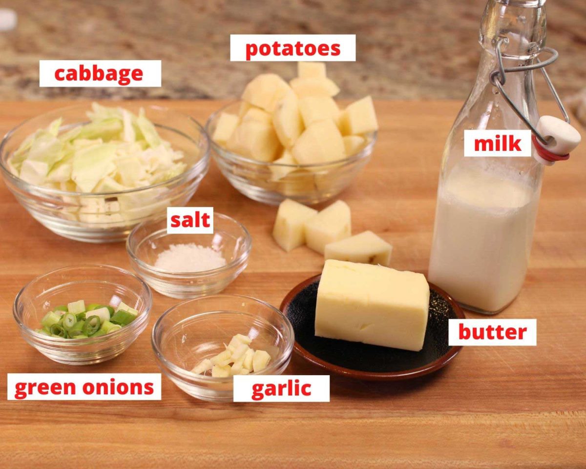 small bowls of diced potatoes, cabbage, salt, garlic, butter, and milk on a brown wooden cutting board.