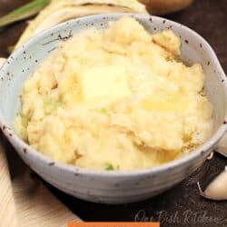 a blue bowl filled with colcannon next to fresh cabbage and a russet potato.