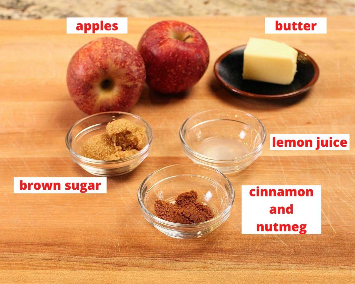two apples, butter, brown sugar, lemon juice, and cinnamon in bowls on a brown cutting board.