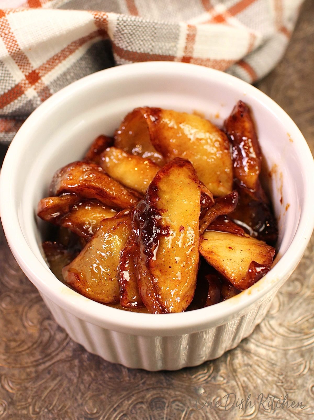 a small white bowl filled with fried apples on a silver tray next to an orange and white napkin.