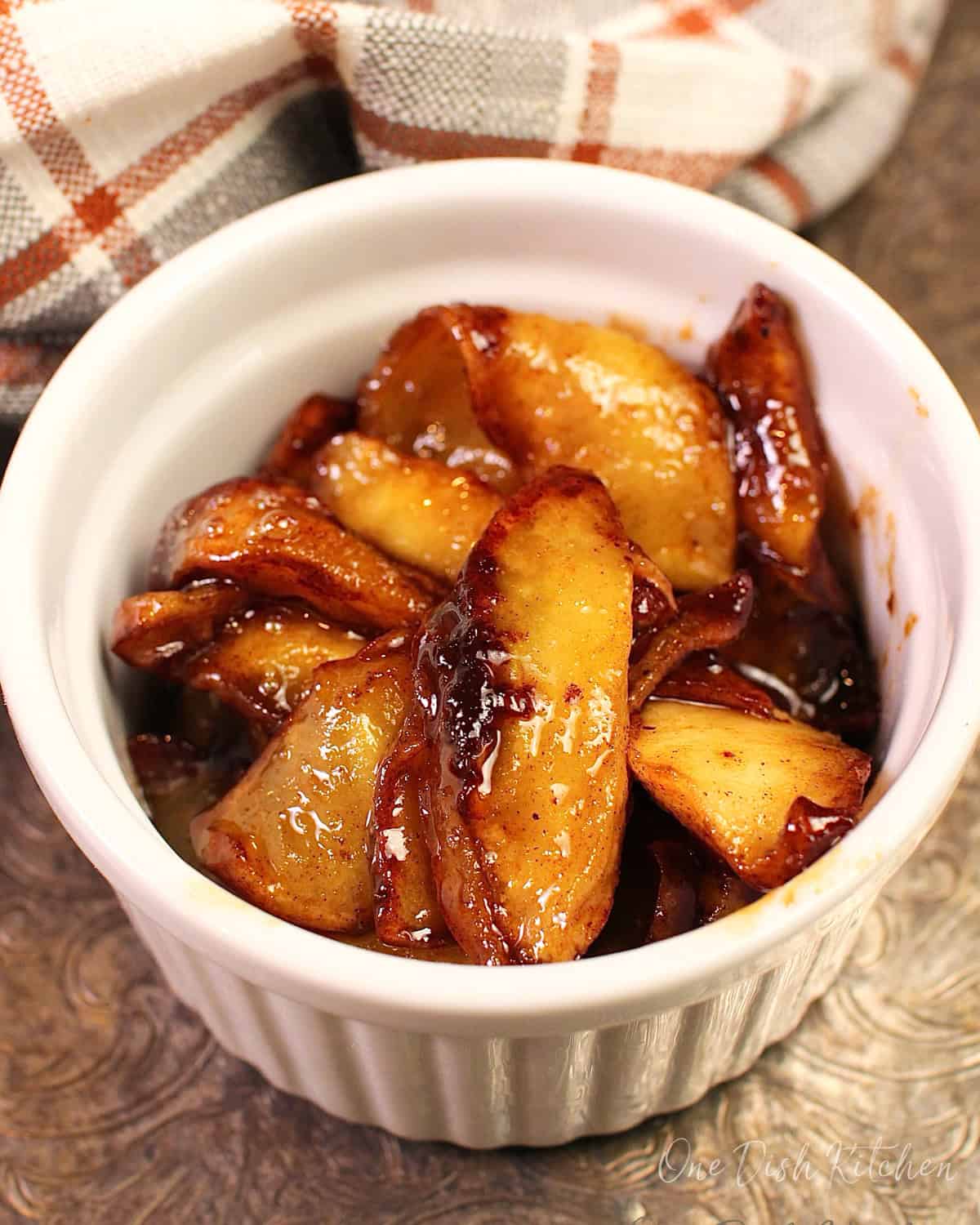 a small white bowl filled with fried apples on a silver tray next to an orange and white napkin.