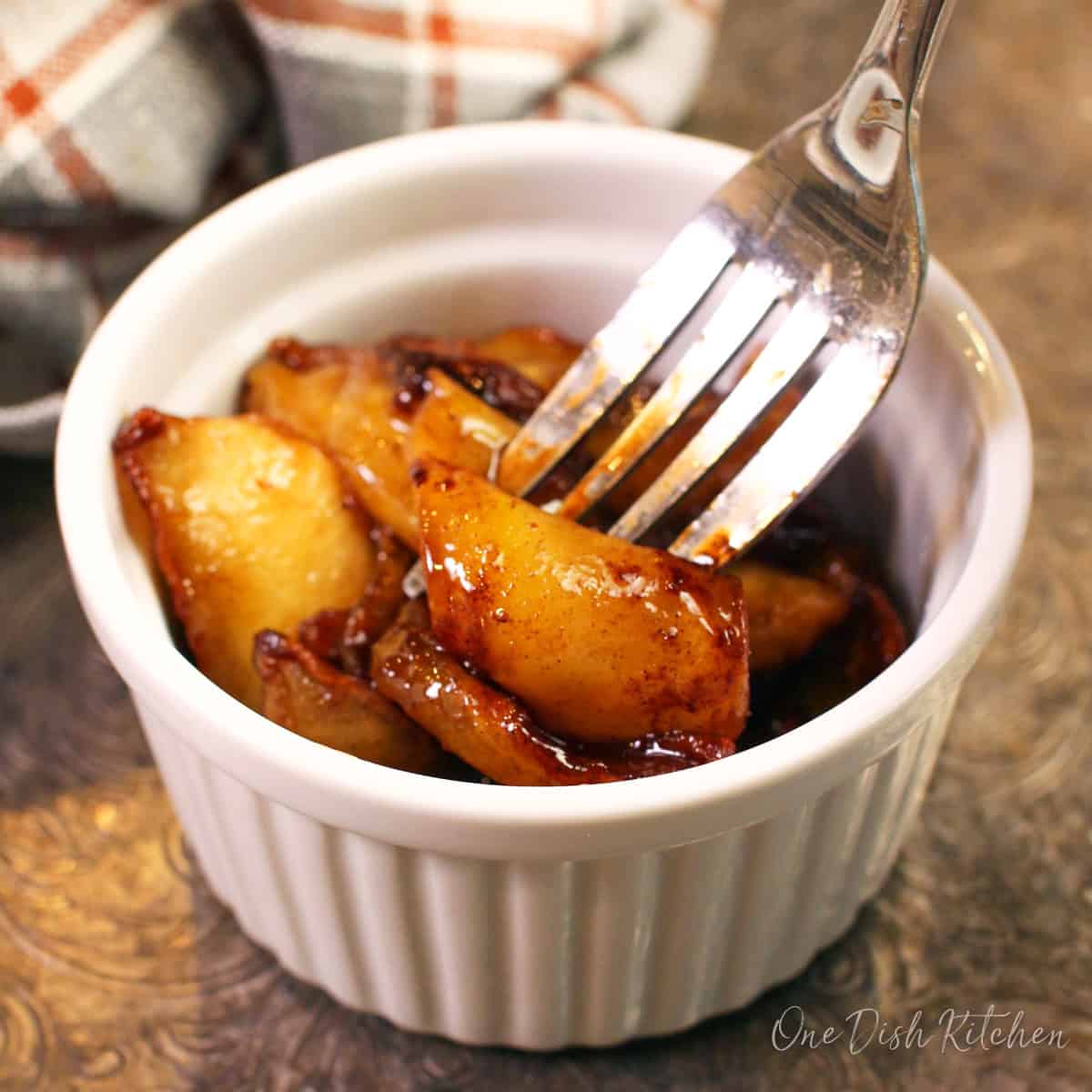 soft, fried cinnamon apples on a fork next to a white and orange plaid napkin.