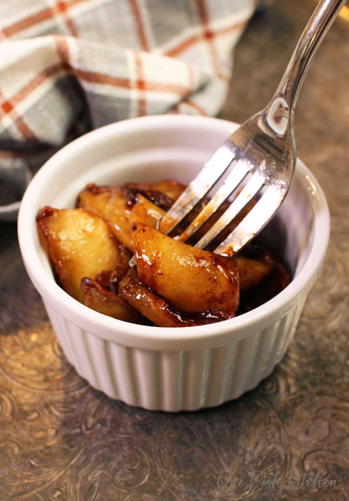 soft, fried cinnamon apples on a fork next to a white and orange plaid napkin.