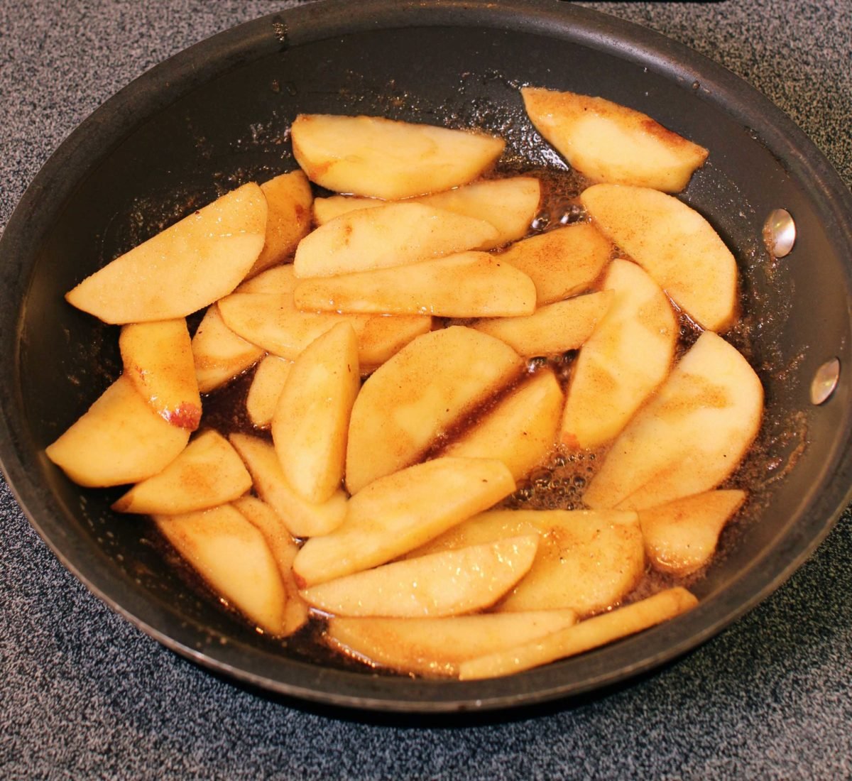 apple slices tossed with melted butter and brown sugar in a frying pan.
