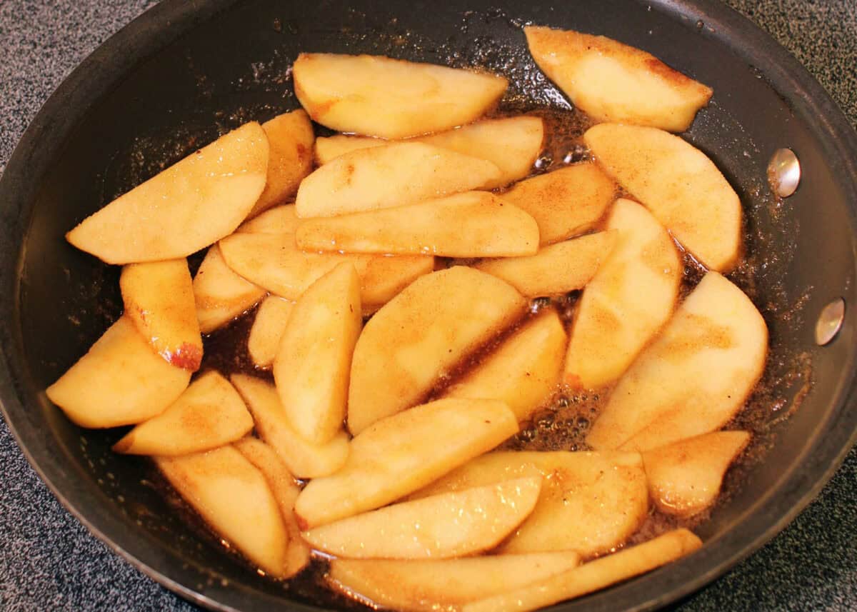 apple slices tossed with melted butter and brown sugar in a frying pan.
