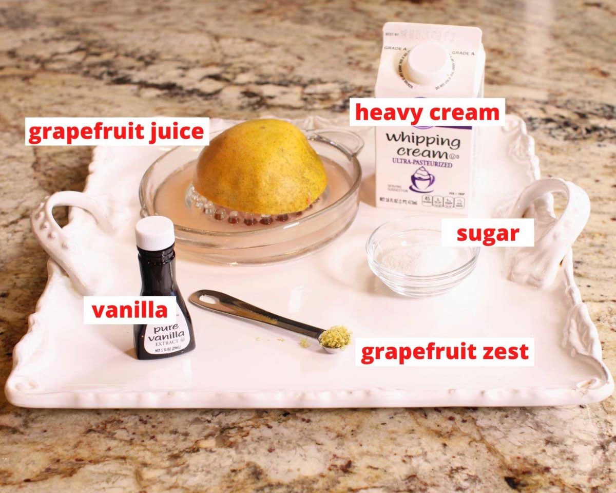 cream, half of a grapefruit, vanilla, and sugar on a white tray sitting on a brown granite kitchen counter.