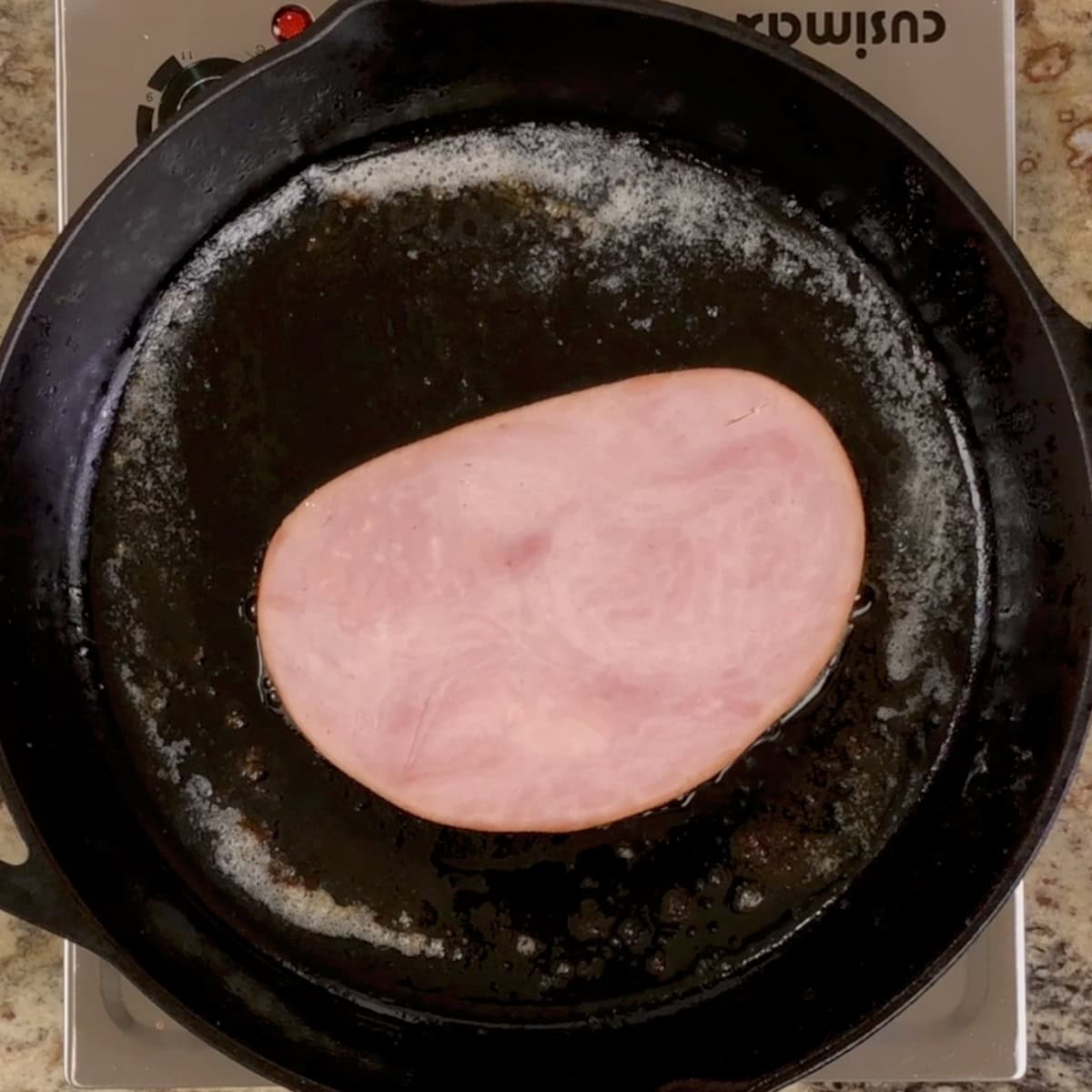 a ham steak cooking in a skillet.