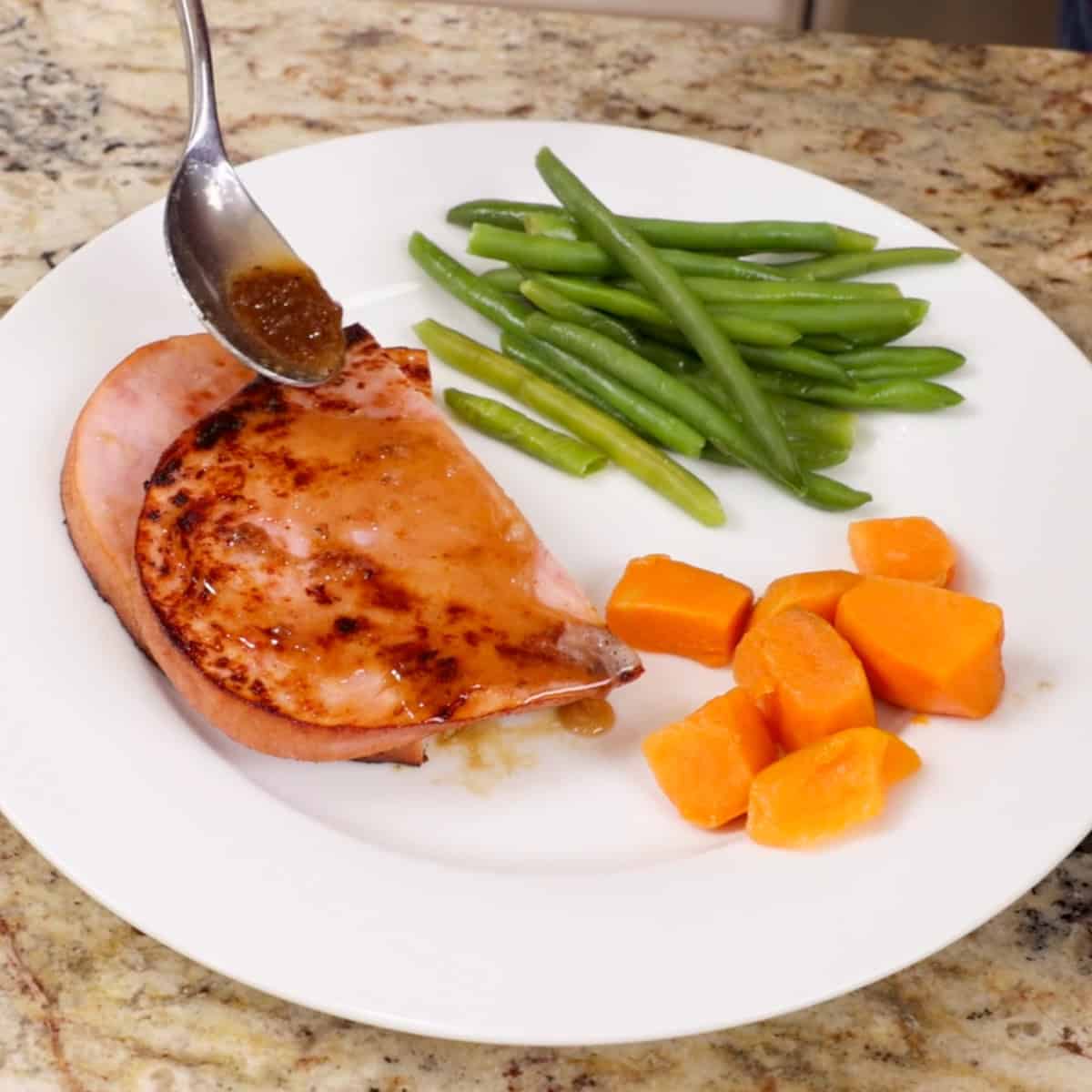 a brown sugar glaze poured over a ham steak on a white plate.