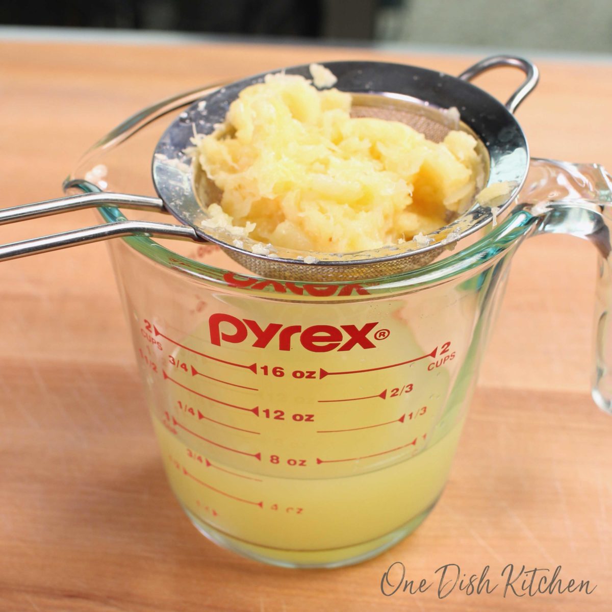 a pyrex measuring cup with a little pineapple juice in the bottom and a strainer filled with crushed pineapples resting over the top.