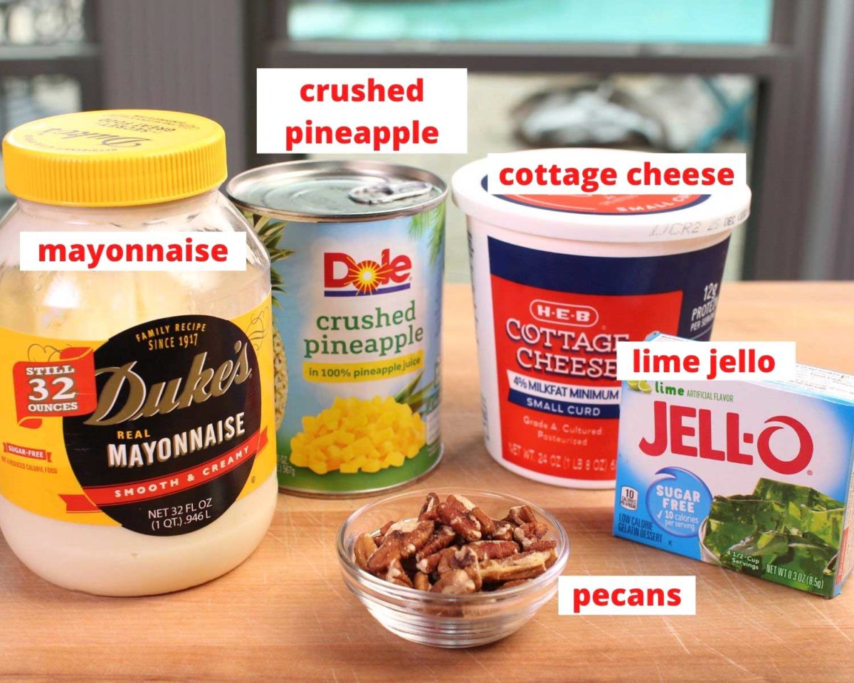 mayonnaise, a can of pineapples, lime jello box, cottage cheese carton, and a bowl of pecans on a brown wooden cutting board.