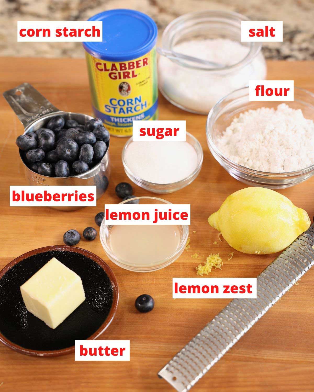 butter, blueberries, lemons, flour, and cornstarch on a wooden cutting board.
