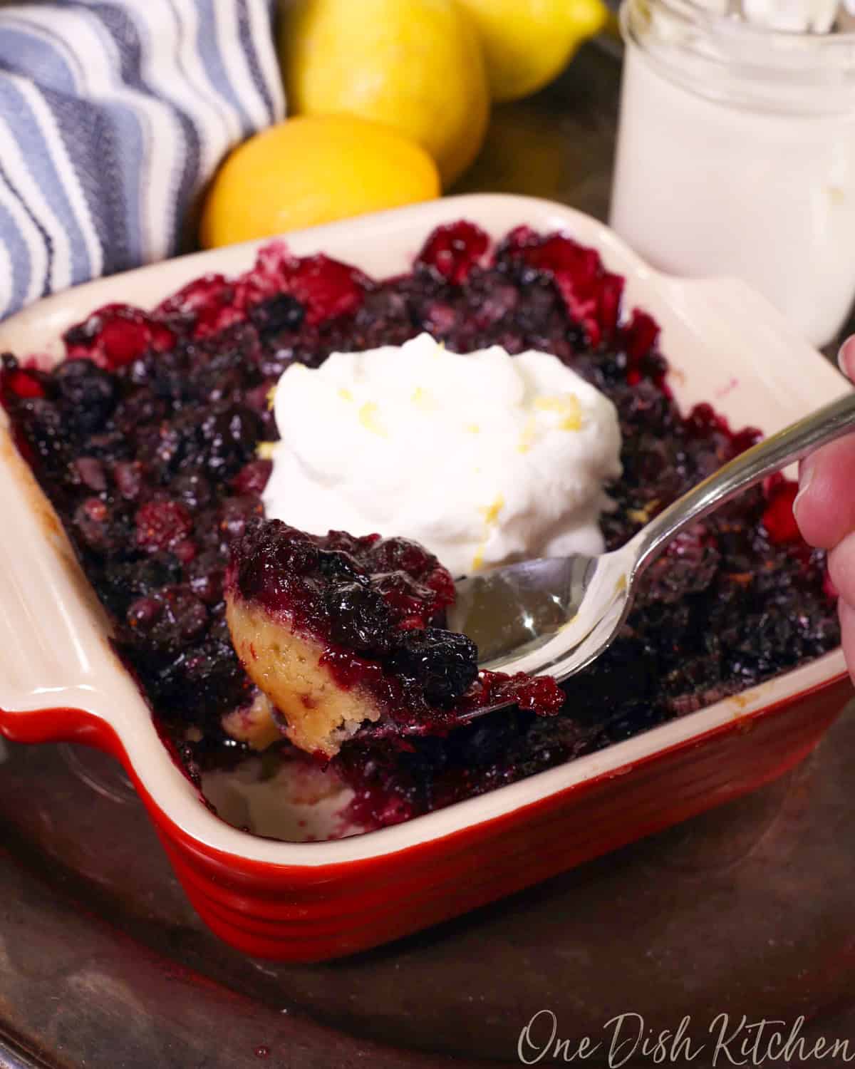 a small blueberry pie topped with whipped cream and a spoon on the side.