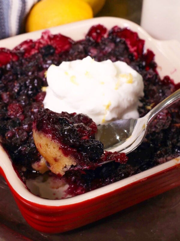 a small blueberry pie topped with whipped cream and a spoon on the side.