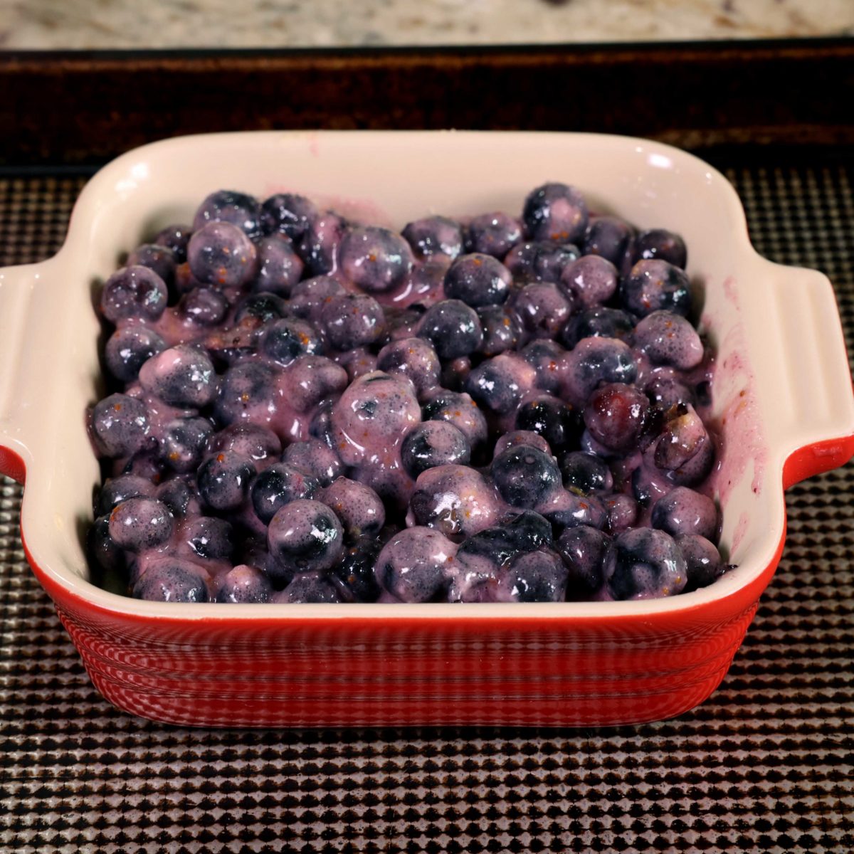 blueberries tossed with flour and juice on top of a pie crust in a red baking dish.