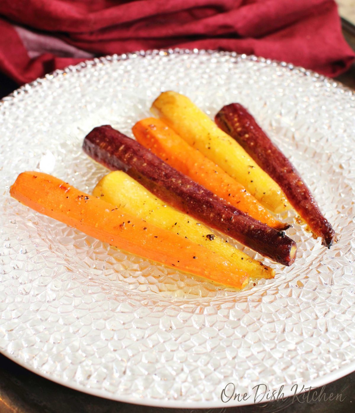 colorful carrots on a white plate next to a red napkin.