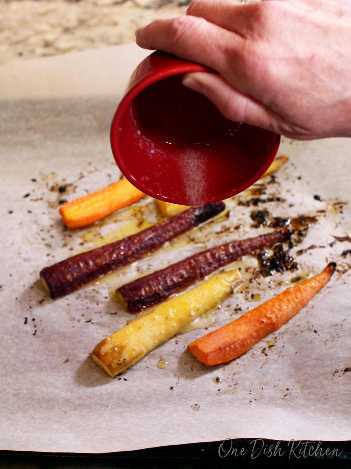 melted butter in a small red bowl being poured over baked carrots.