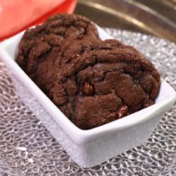four double chocolate chip cookies in a mini white loaf pan next to an orange napkin