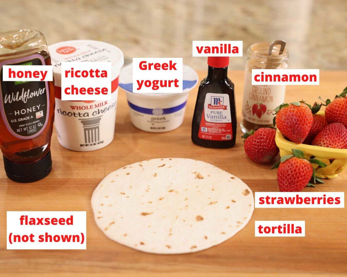 honey, cheese, yogurt, vanilla, spices, fruit, and a tortilla on a brown wooden cutting board.