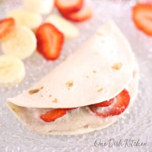 a strawberry quesadilla on a white plate next to sliced bananas and strawberries