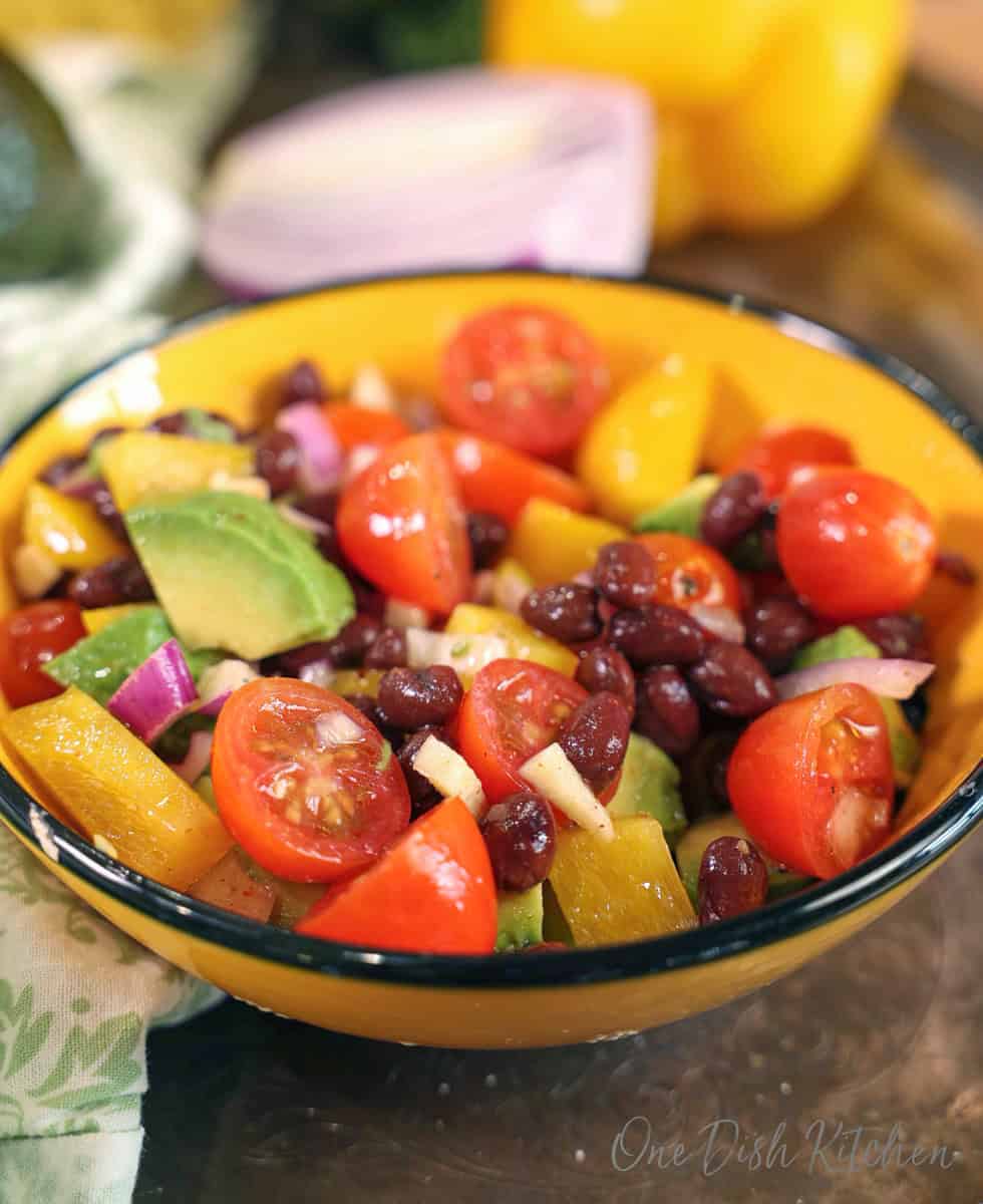 a bowl filled with a guacamole salad topped with black beans and garlic on a silver tray.
