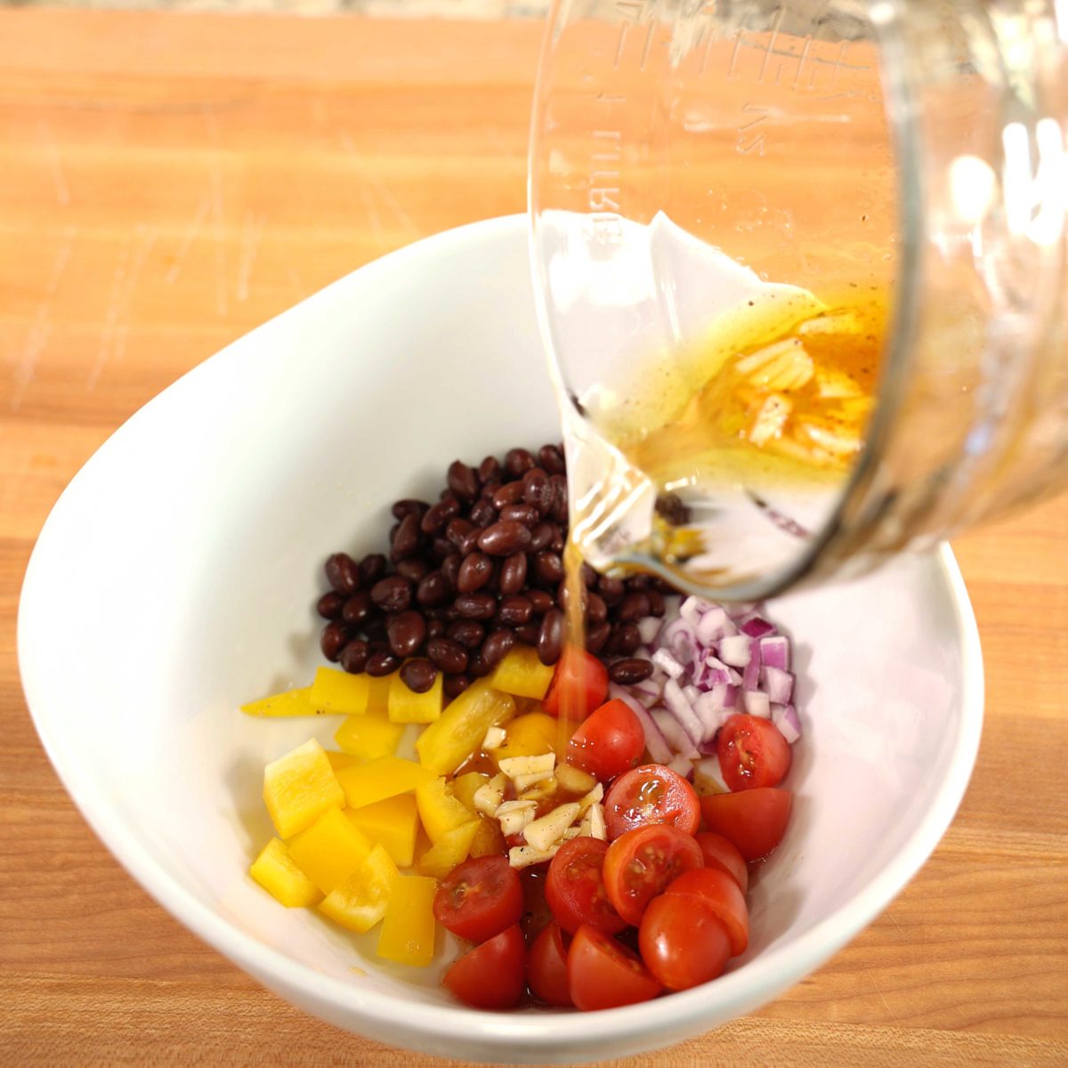 dressing poured over a bowl of tomatoes, yellow pepper, black beans and red onions.
