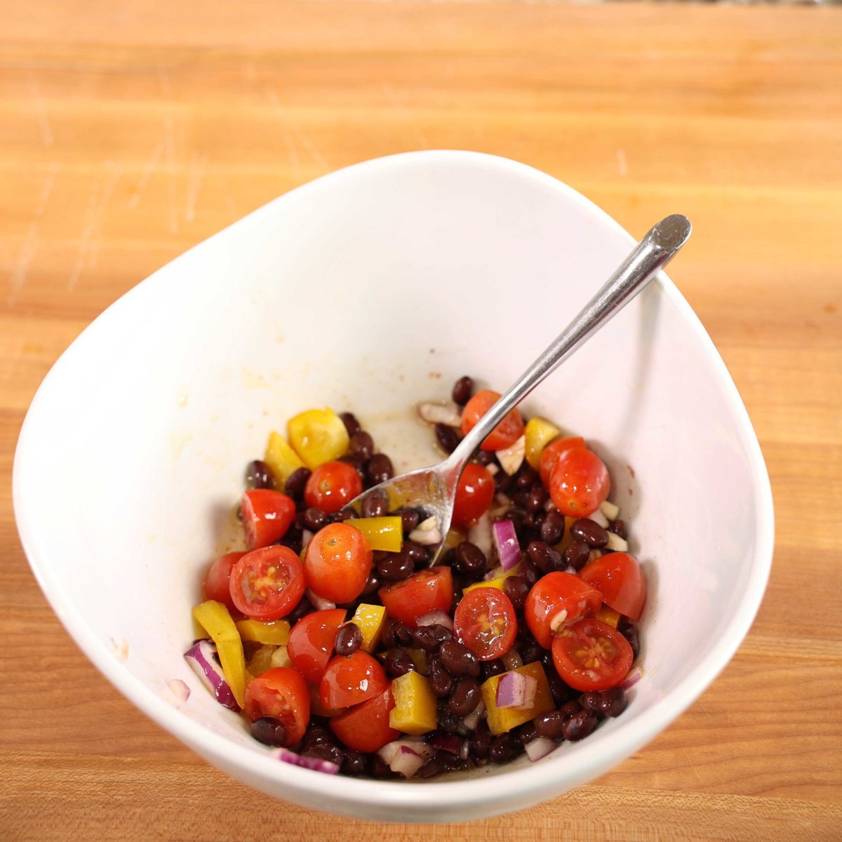 black beans, tomatoes, and yellow peppers on a white bowl with a spoon on the side.