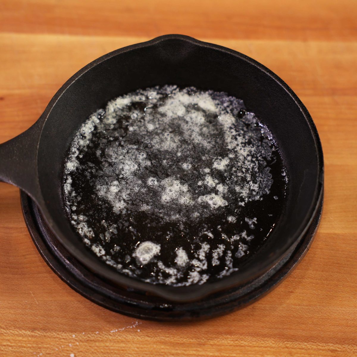a mini cast iron skillet filled with melted butter on a brown cutting board.