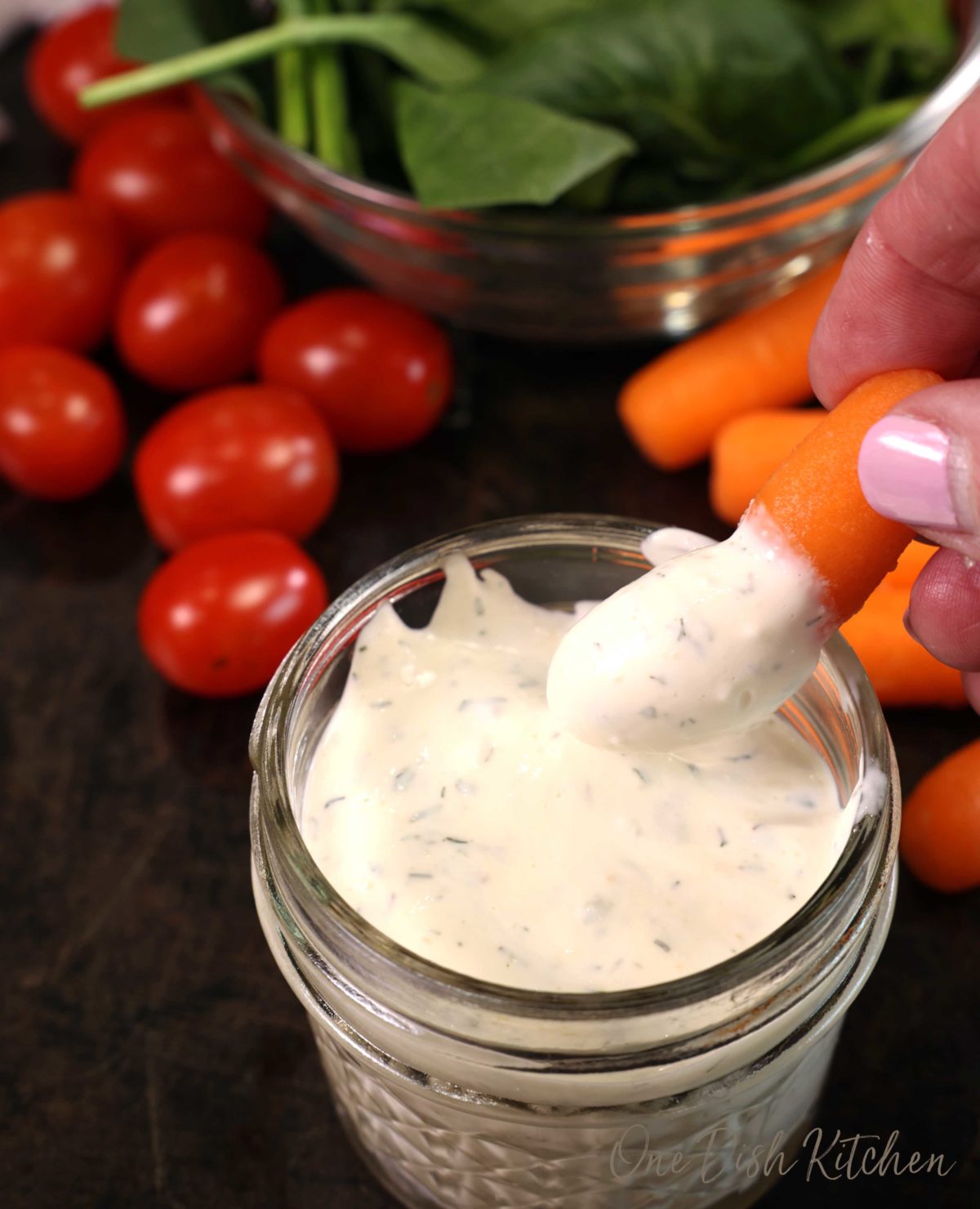a small jar of homemade ranch dressing with a carrot dipped in the corner next to cherry tomatoes.