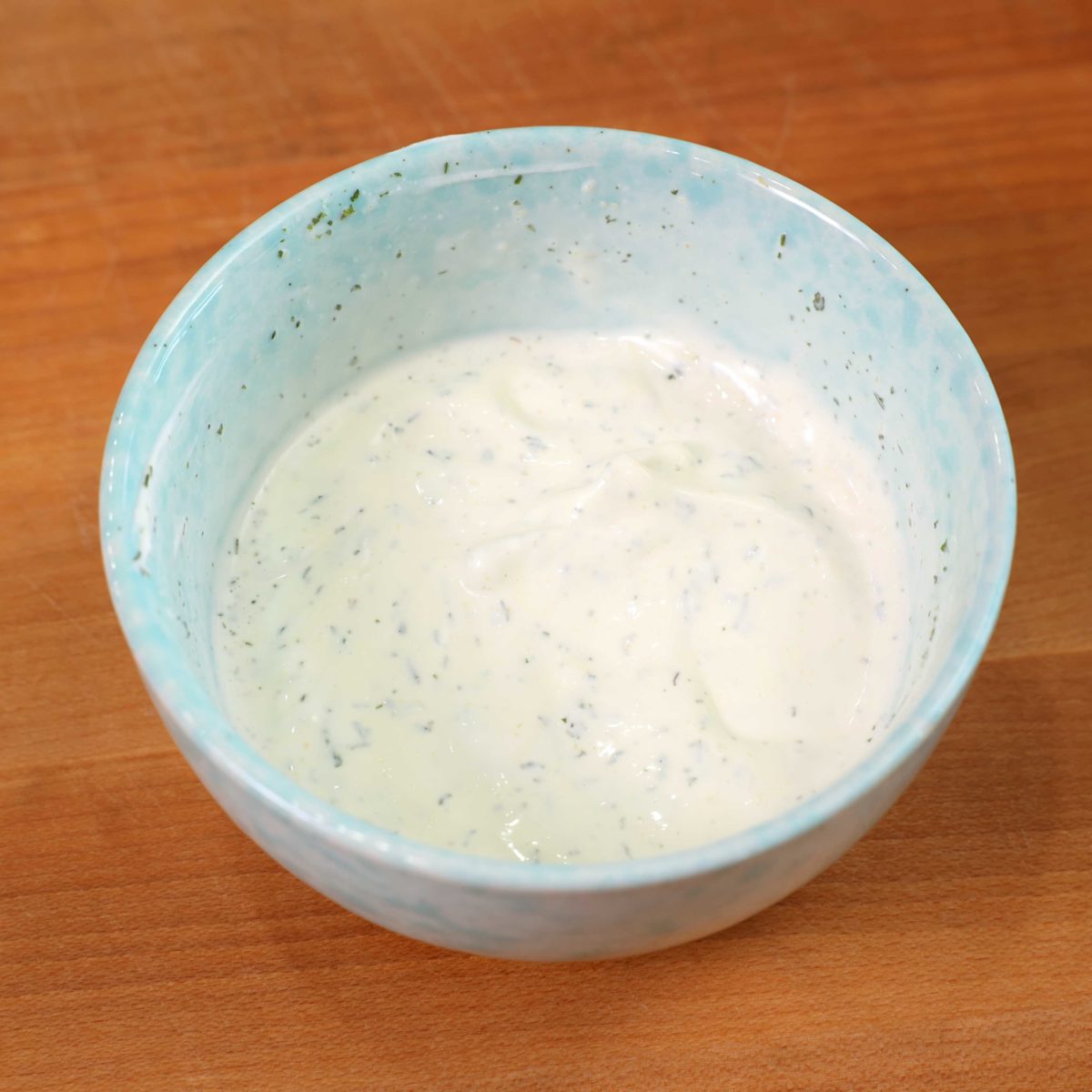 a small amount of ranch dressing in a blue bowl on top of a wooden cutting board.