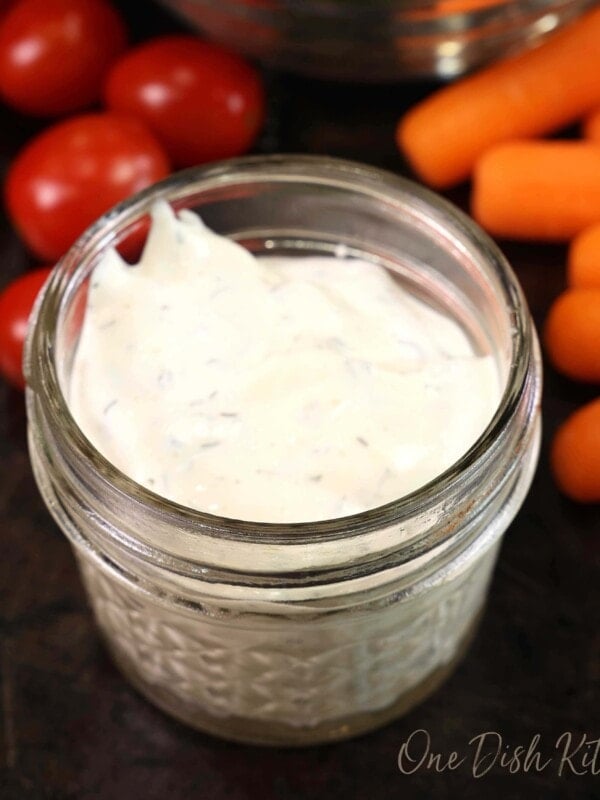 a small mason jar filled with ranch dressing on a black table next to carrots and grape tomatoes