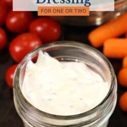 a small jar of ranch dressing surrounded by tomatoes and carrots.
