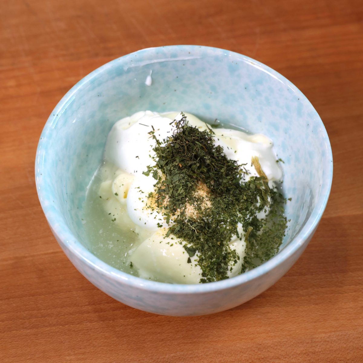 a blue bowl filled with mayonnaise, sour cream, lemon juice, and dried herbs.