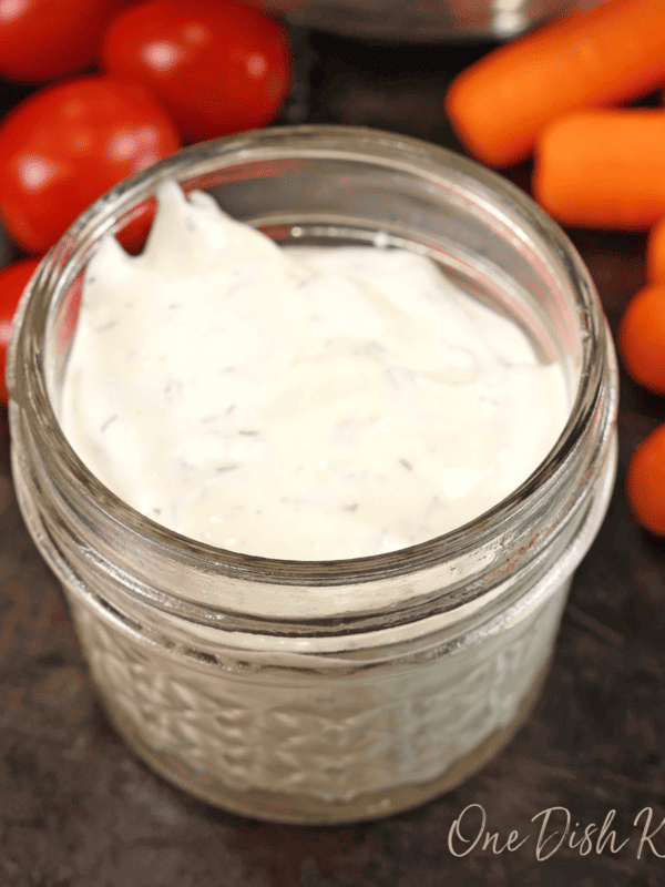 a small mason jar filled with ranch dressing on a black table next to carrots and grape tomatoes.