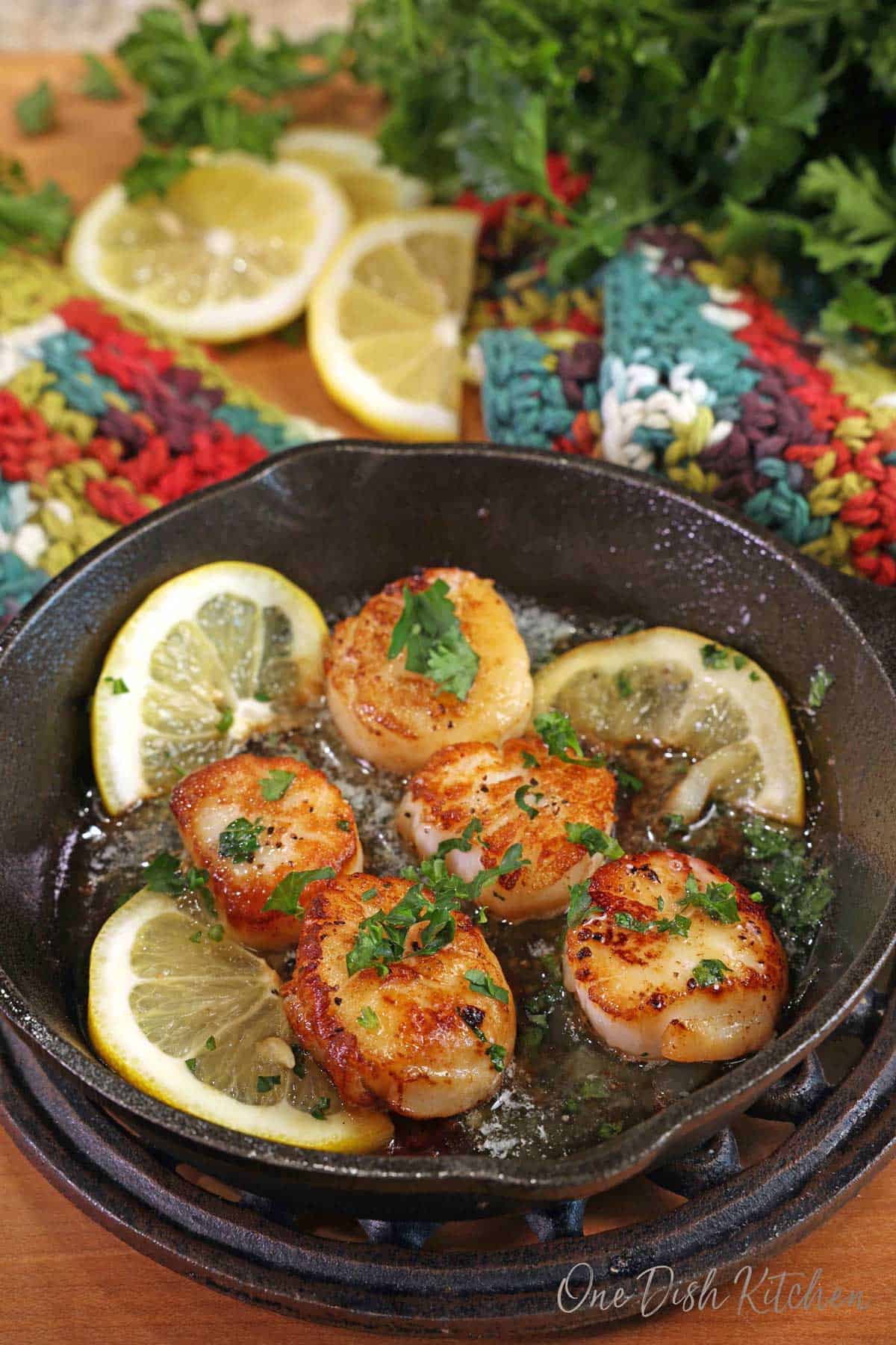five pan seared scallops in a mini cast iron skillet next to sliced lemons and topped with chopped parsley.
