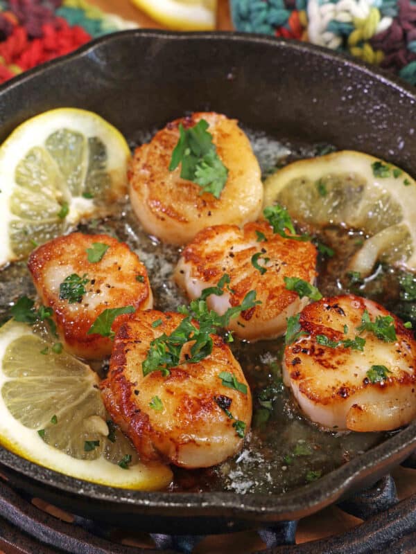 5 cooked scallops in a cast iron skillet surrounded by lemon slices.